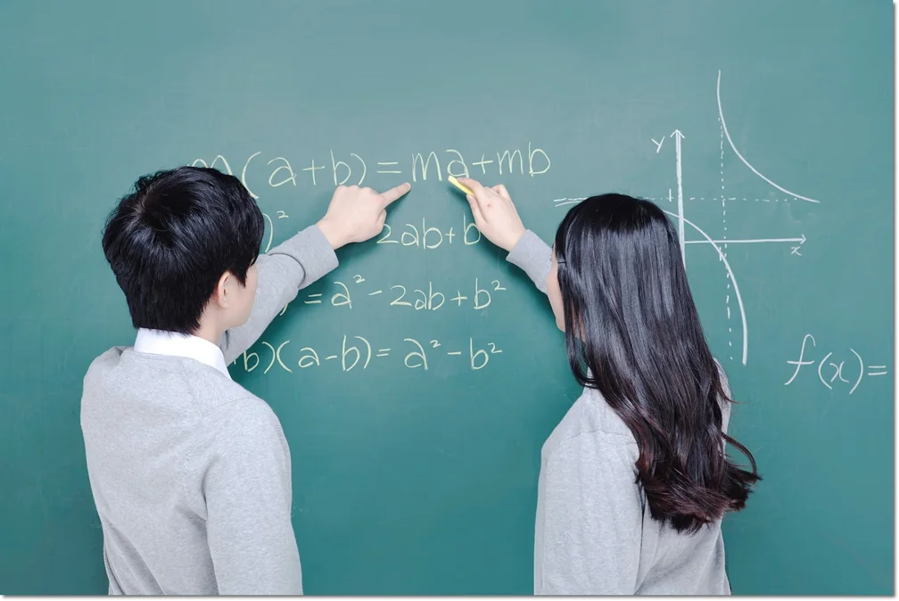 칠판의 수식을 함께 가리키며 살펴보는 두 학생