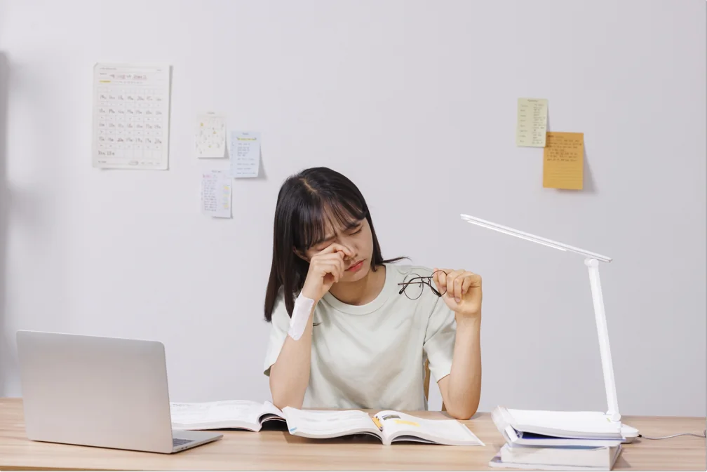 노트북과 펼친 책 앞에서 생각하는 학생